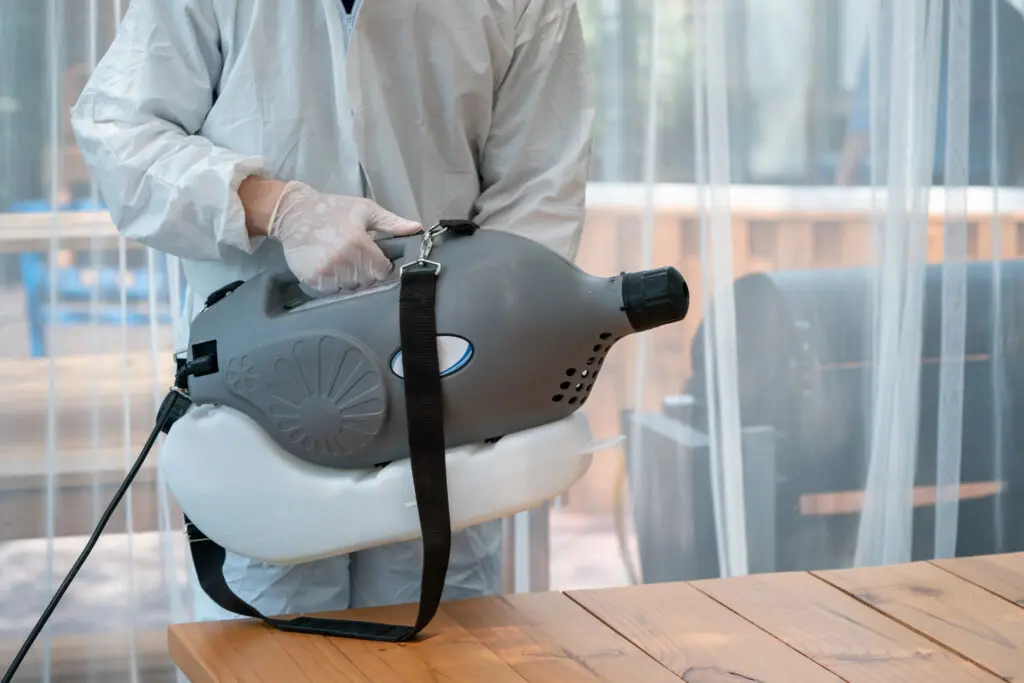 "Professional technical man in prevention suit sprays sterilizing solution"nby electrical spray machine in the indoor glass hourse room."