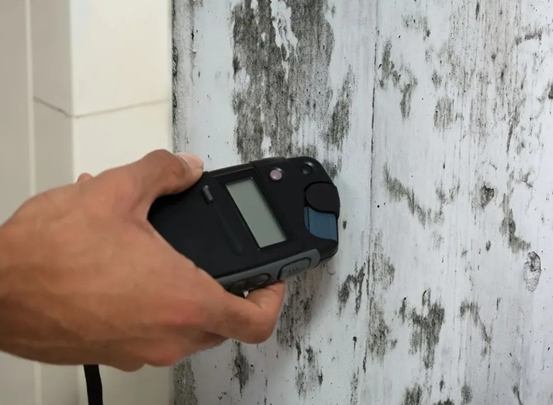 Hand measuring moisture on a wall surface.